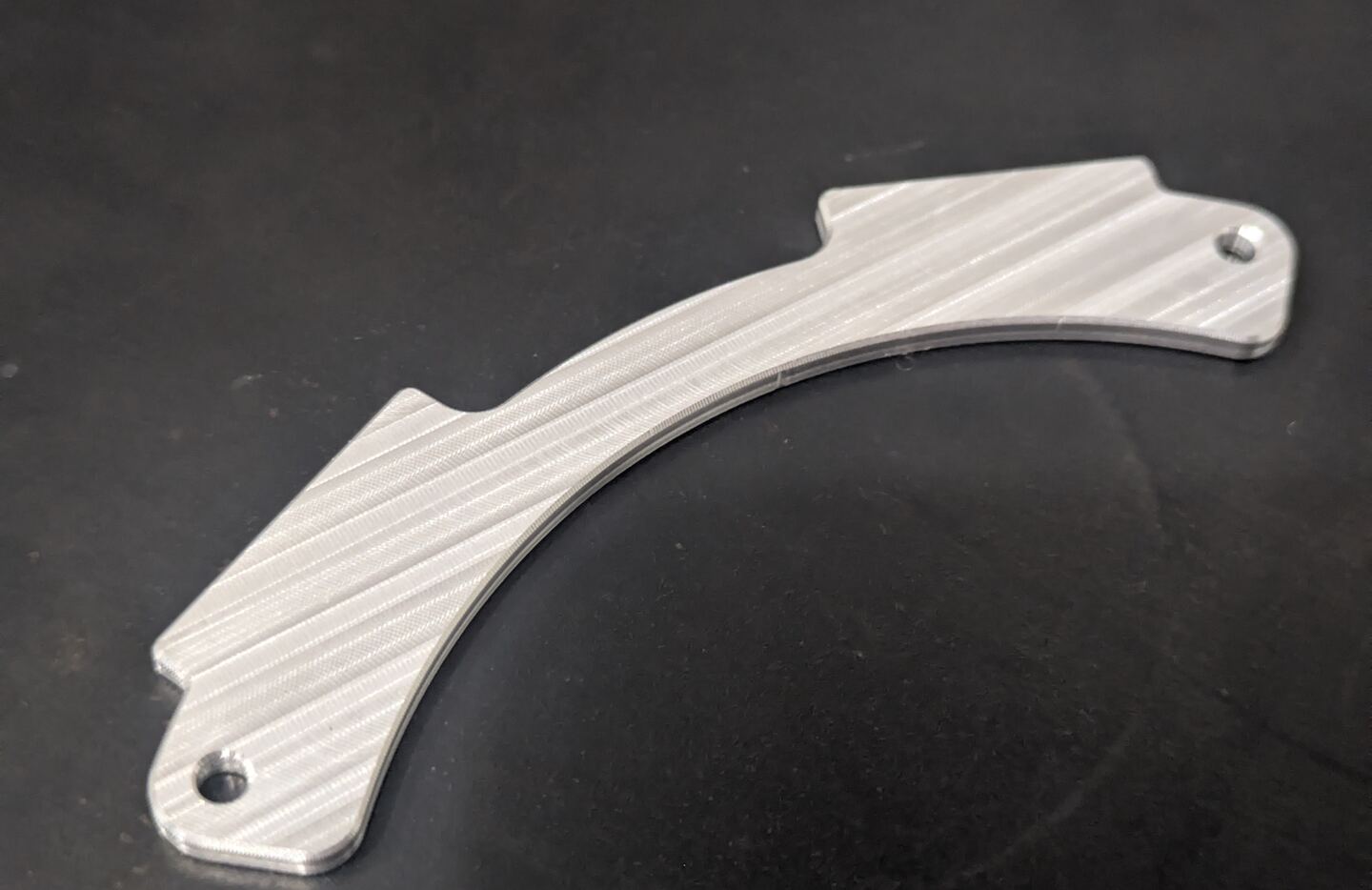 Curved machined metal component on a dark work surface